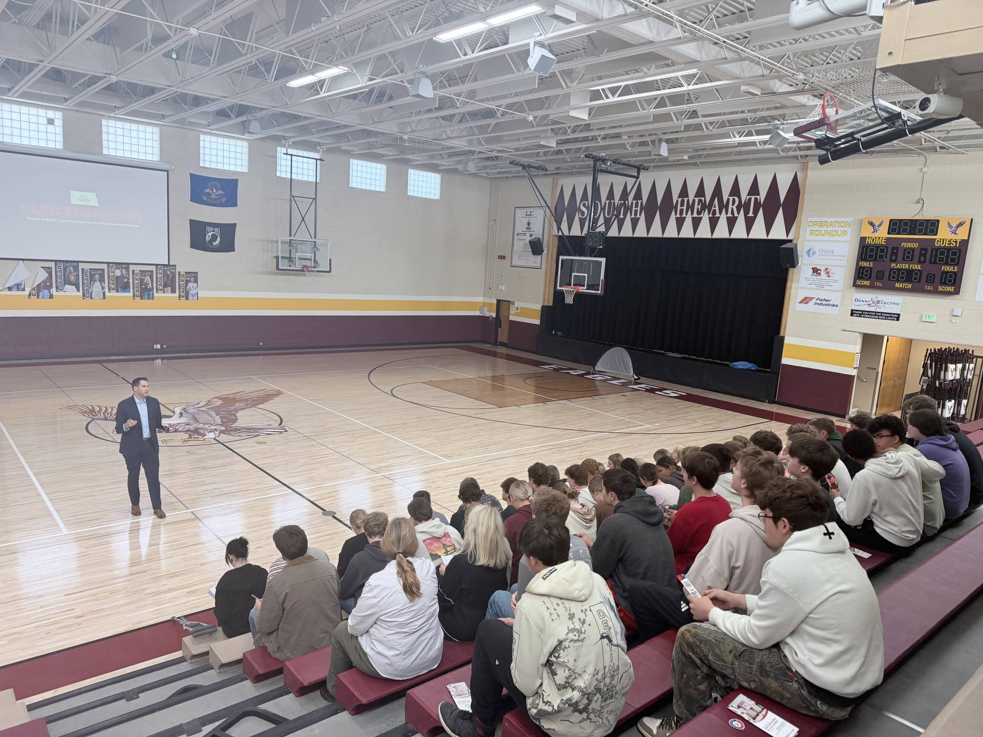 Secretary Howe talking to high school students who are sitting on bleachers in a gymnasium.